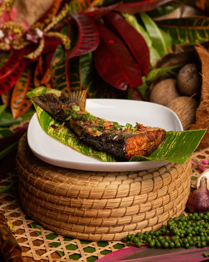 Ikan patin goreng kunyit bertabur bawang goreng dan daun bawang, di atas daun dalam pinggan putih