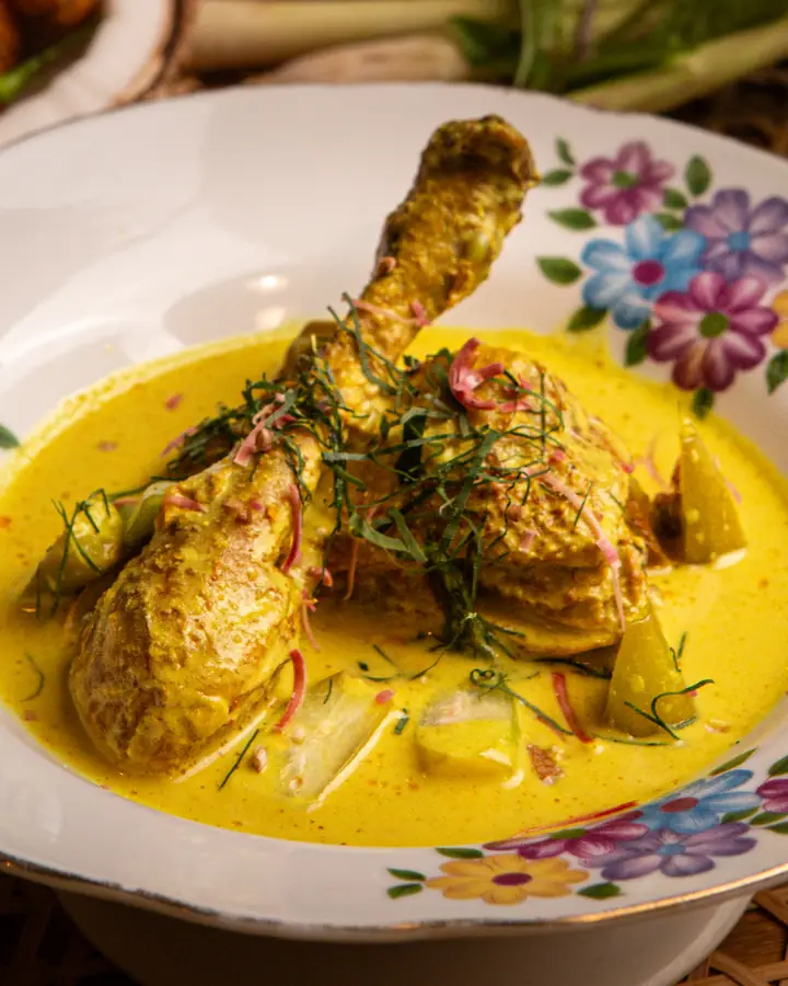 Gulai lemak cili api ayam kampung, peha ayam dalam kuah santan kuning bertabur daun kesum, dalam pinggan bercorak bunga