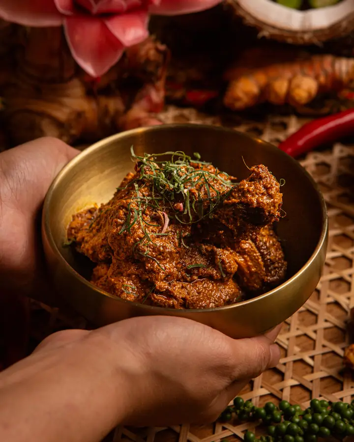 Rendang itik salai dalam mangkuk tembaga, bertabur hirisan daun kunyit